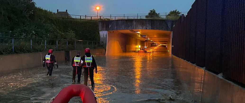 Feuerwehrmänner stehen vor einem Tunnel, der nach einem Unwetter überflutet ist.