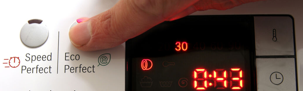 Anzeige einer Waschmaschine, Finger drückt auf einen Knopf mit der Aufschrift 