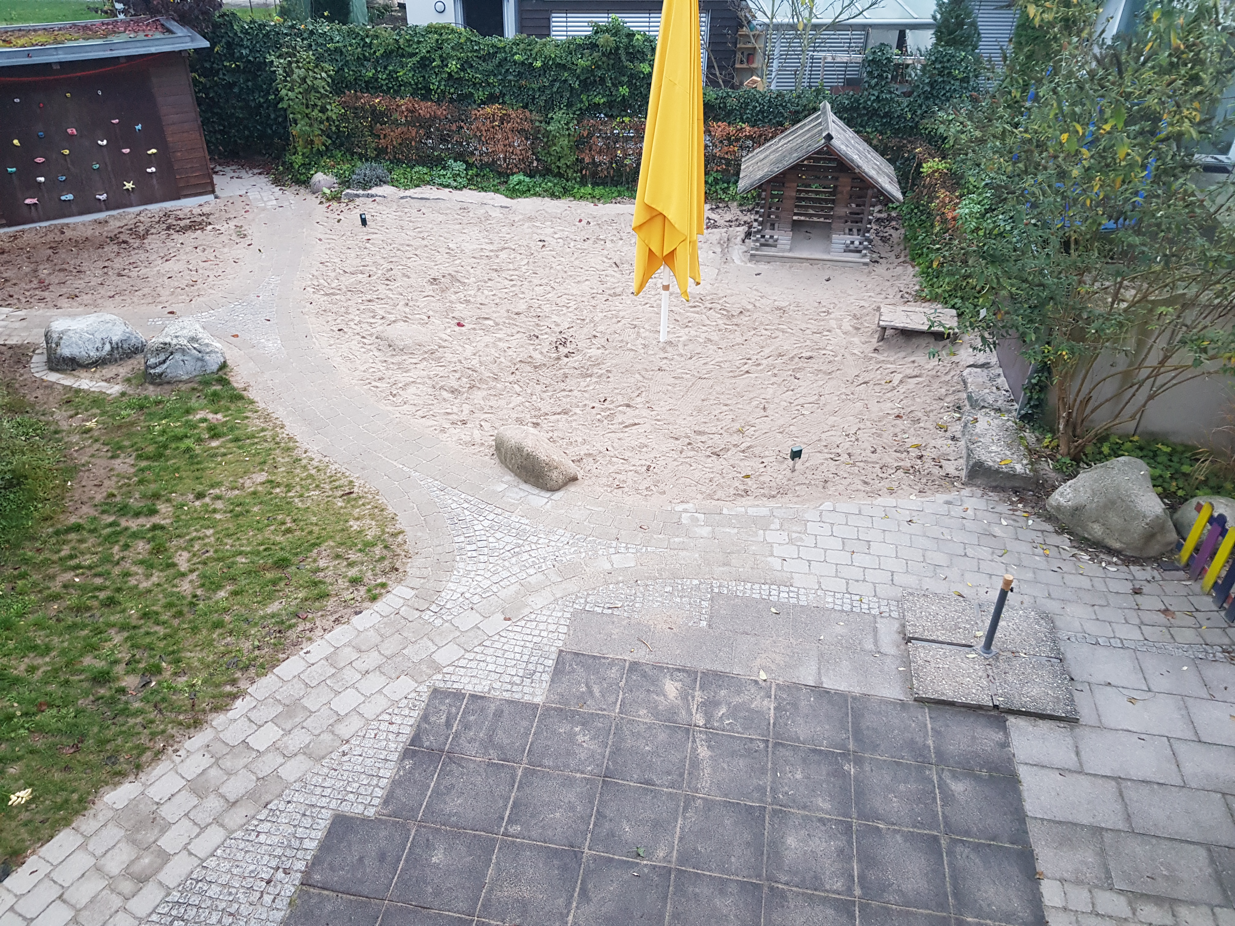 Hier sieht man den Sandkasten mit einem gelben Sonnenschirm, welcher nicht aufgespannt ist.