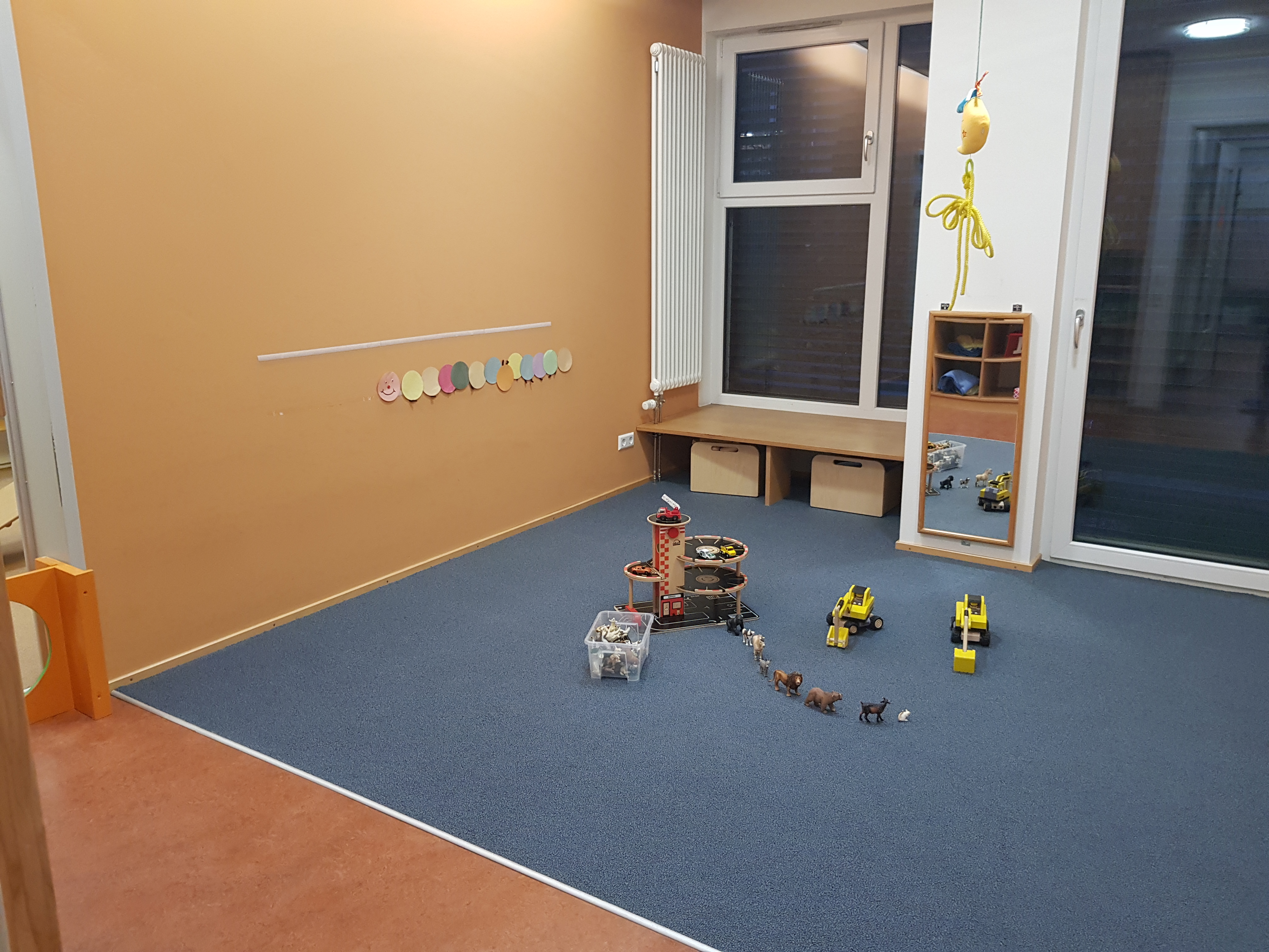 Das Bild zeigt eine Fläche, welche die Krippenkinder zum spielen und bauen benutzen. Es ist ein Parkhaus, Tiere aus Gummi und zwei gelbe Bagger abgebildet.