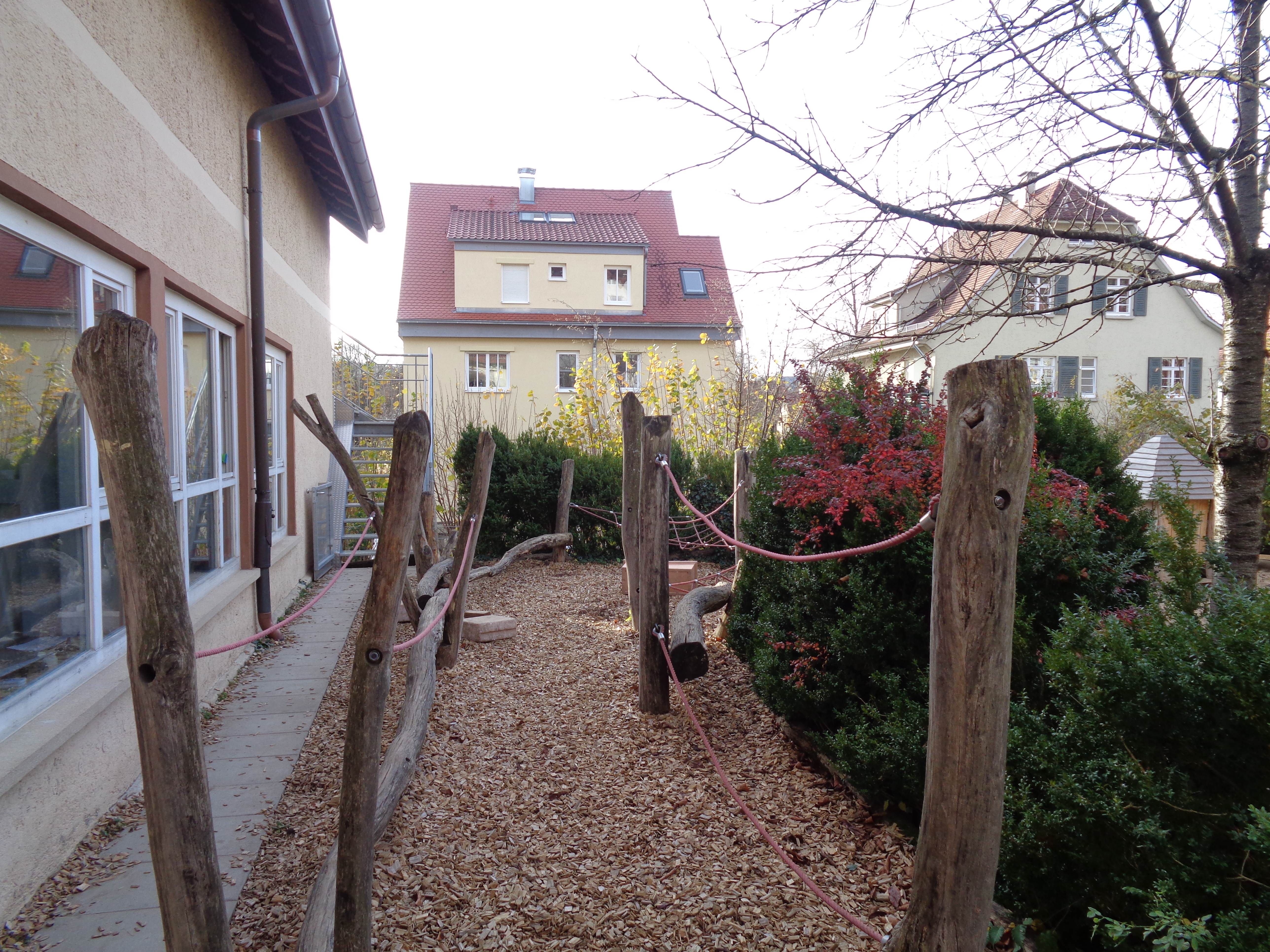 Es sind links neben dem Kinderhaus verschiedene Kletter- und Balanciermöglichkeiten aus Holz und Seilen zu sehen.