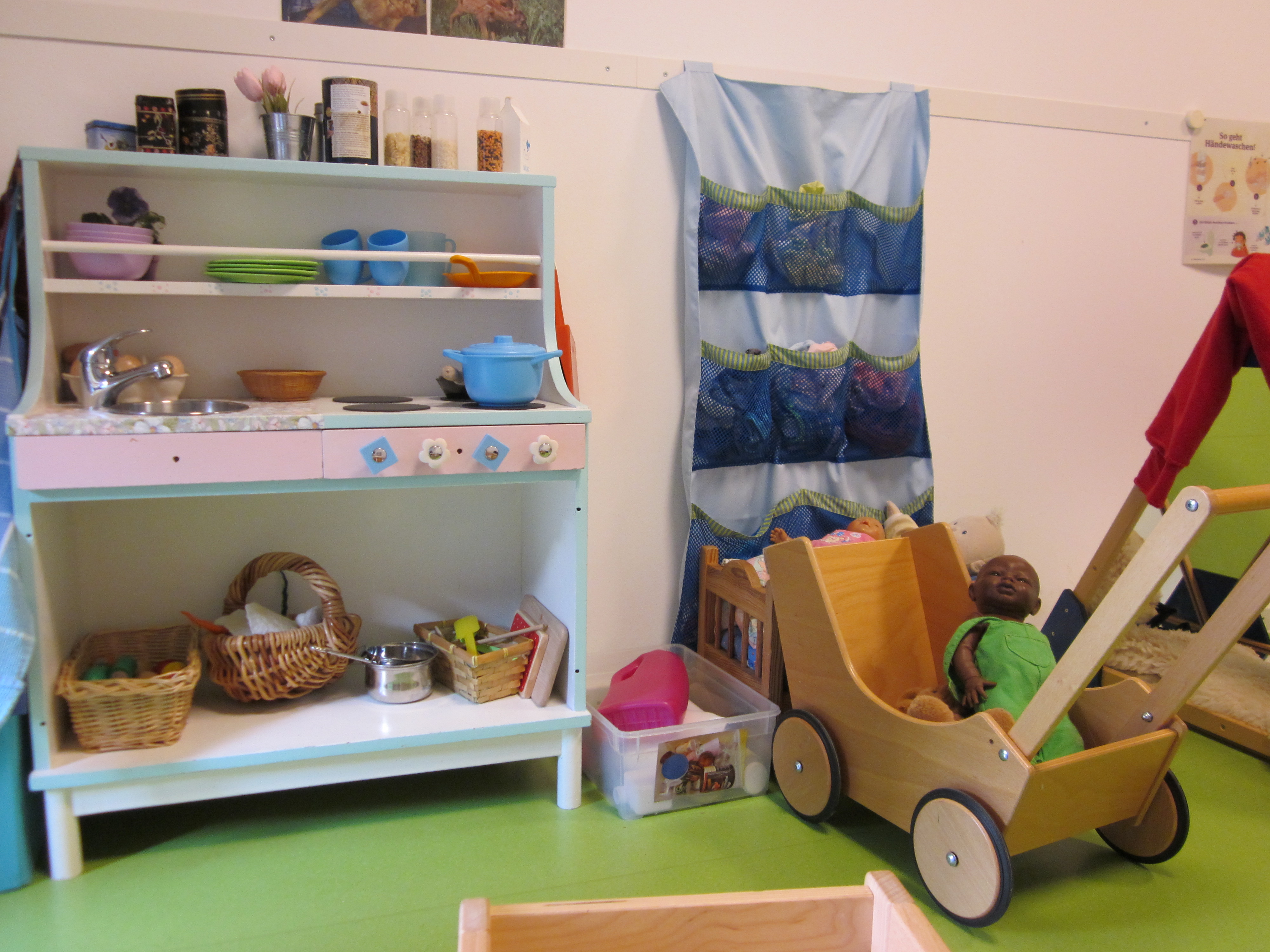 Auf dem Bild ist eine Kinderküche und daneben ein Puppenwagen zu sehen.