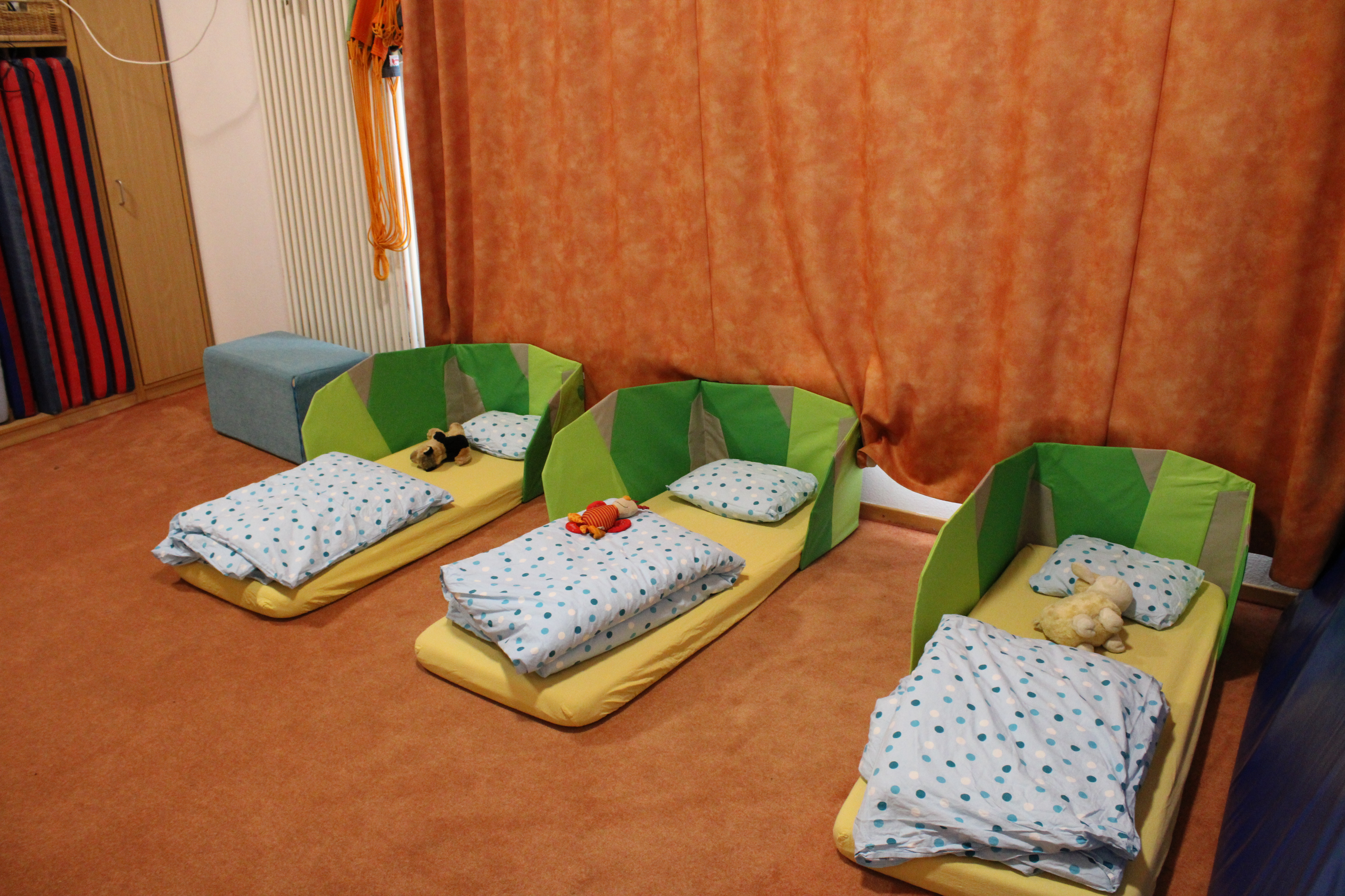 Hier ist ein Teil des Schlafraums zu sehen. Es liegen drei Matratzen mit gelben Spannbetttuch auf dem Boden. Es gibt blau gepunktete Bettwäsche.