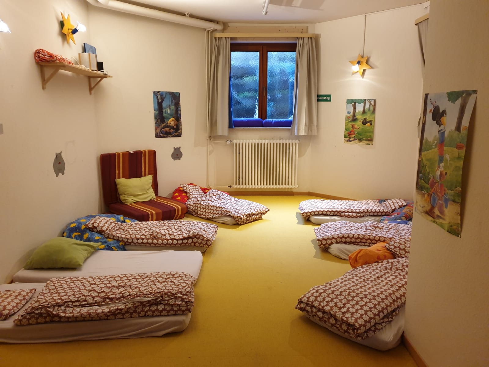 Hier ist der Schlafraum zu sehen. Es liegen Matratzen auf dem Boden, mit weißen Spannbetttüchern und rot weißer Bettwäsche.