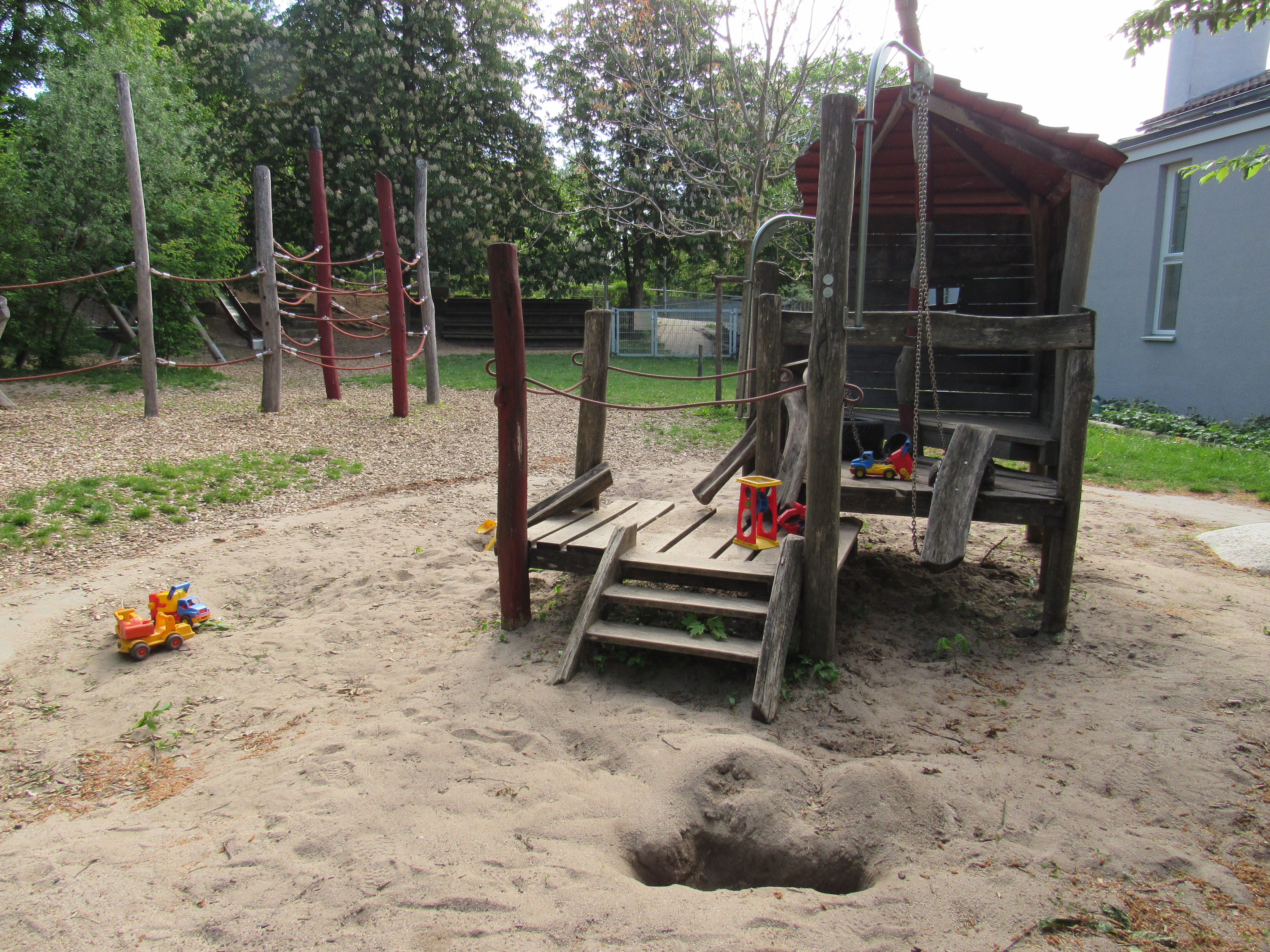 Das Bild zeigt ein Spielhaus aus Holz in einem Sandkasten.