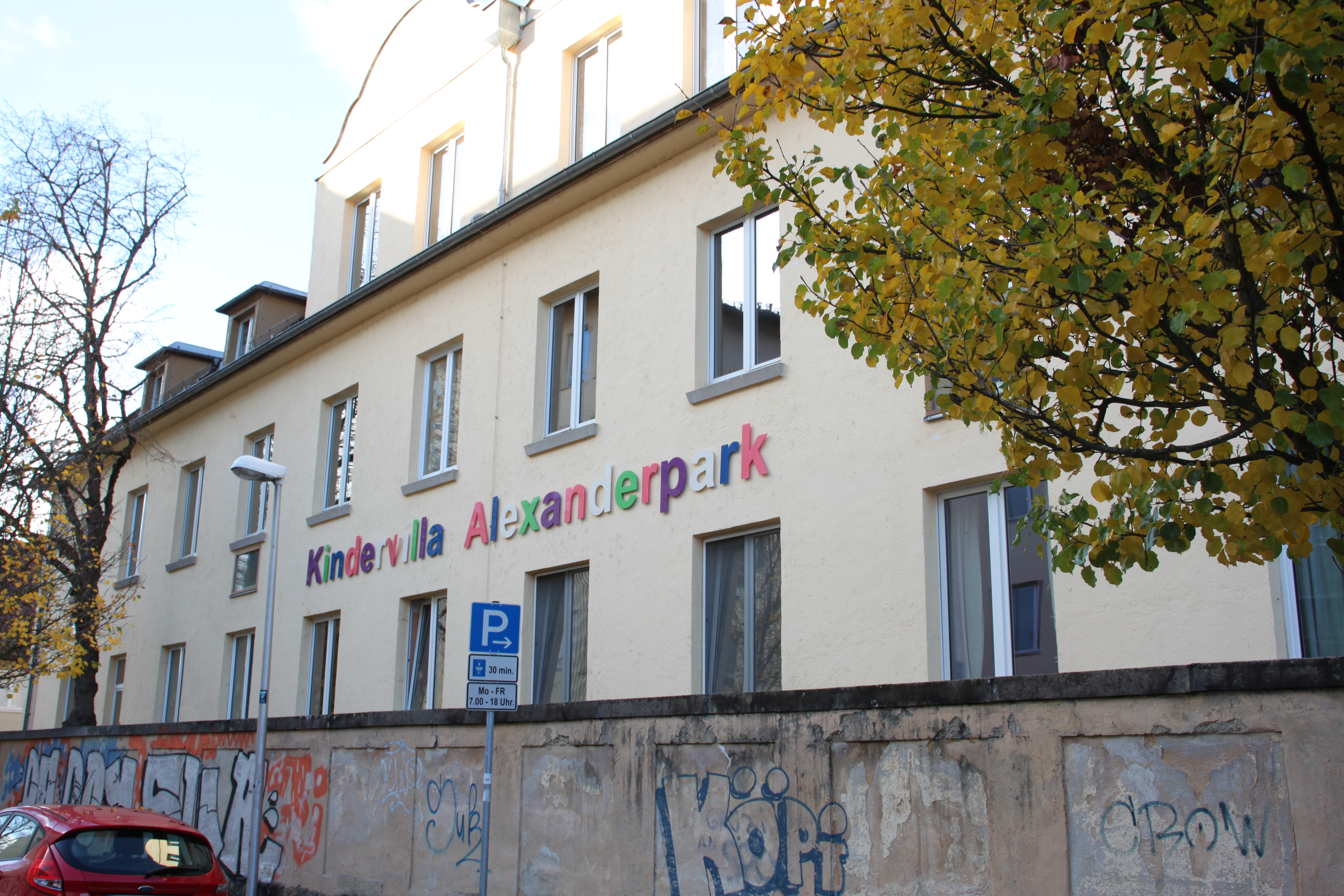 Auf dem Bild ist die Kindervilla mit Schriftzug abgebildet. Im Vordergrund ist eine Mauer mit Graffiti.
