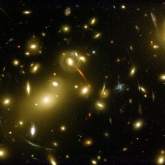 Die Gravitationswirkung des Galaxienclusters Abell 2218, das mehrere Tausend Galaxien umfasst, zwingt Lichtstrahlen auf Bahnen, die denen bei einer Sammellinse ähneln. Bilder dahinterliegender Galaxien können dadurch verzerrt oder vergrößert werden. Bild: NASA, STScI