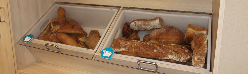 Brote, Baguettes und Brötchen liegen in zwei großen Ablagen unter einer Schutzscheibe (Fairteiler).