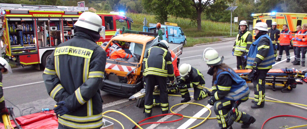 Feuerwehrmänner sind bei einem Verkehrsunfall im Einsatz. Sie untersuchen ein kaputtes Auto.