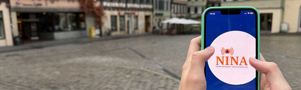 Warn-App Nina auf dem Handy vor der Kulisse des Tübinger Marktplatzes